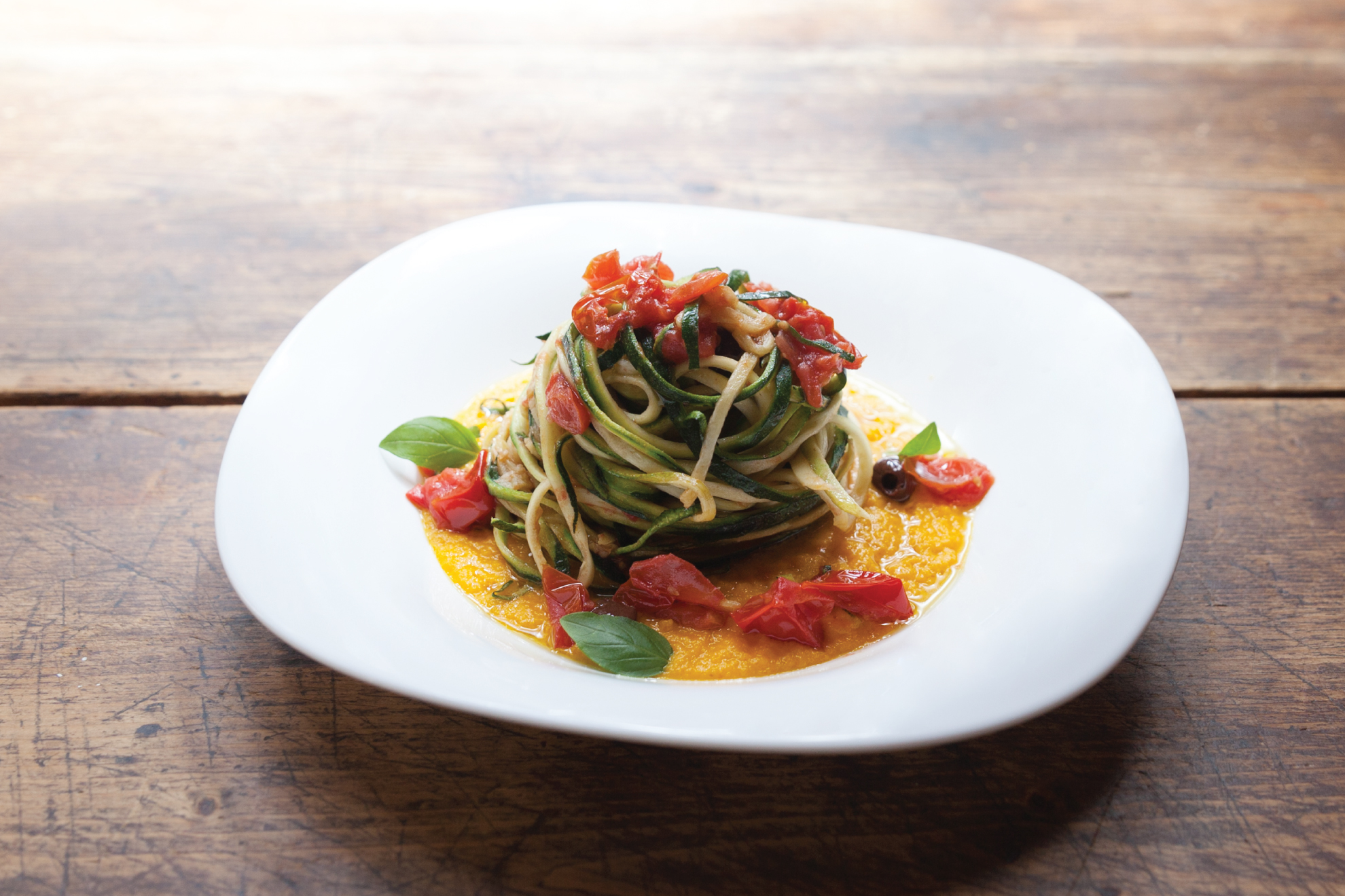 Spaghetti di carote con pomodorini, olive taggiasche su vellutata di brocc